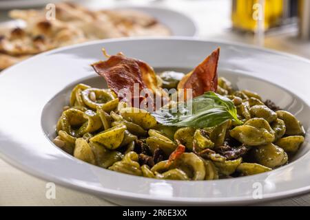 Orecchiette piccola pasta italiana con pesto e croccanti strisce di pancetta. Foto Stock