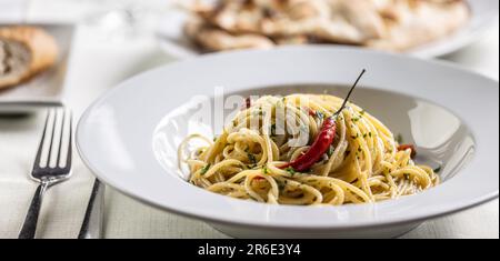 Spaghetti aglio e olio peperoncino con un peperoncino fresco caldo servito in un piatto bianco intenso. Foto Stock