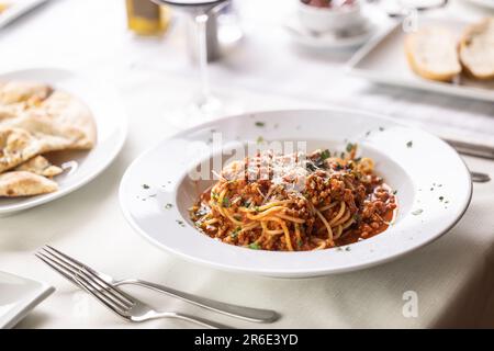 Ristorante che serve spaghetti alla bolognese con formaggio grattugiato su un tavolo bianco. Foto Stock