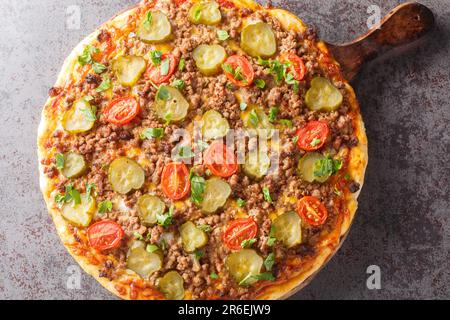 Cheeseburger Pizza è sormontato da una cremosa salsa di hamburger, macinato di manzo, formaggio e sottaceti closeup sul tavolo di legno. Vista orizzontale dall'alto Foto Stock