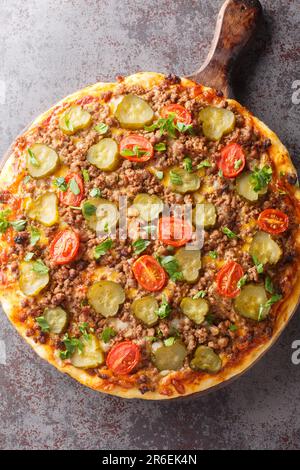 Pizza di hamburger grassi fatta in casa con Pickles di manzo e primo piano di pomodoro sul bordo di legno sul tavolo. Vista verticale dall'alto Foto Stock