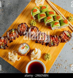 Un primo piano di una deliziosa selezione di sushi servito su un vassoio di legno, con bacchette e un lato di salsa da immersione Foto Stock