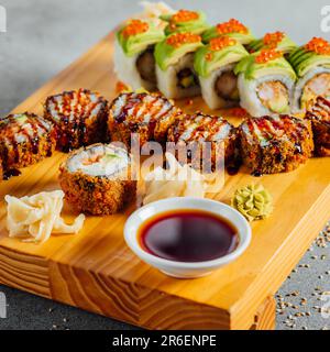 Un vassoio di legno con una varietà di sushi giapponesi e una piccola ciotola di salsa di soia per l'immersione, presentato con un'estetica tradizionale Foto Stock