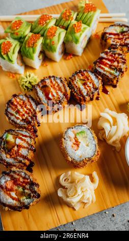 Un piatto ripieno con una varietà di sushi roll e un lato di salsa di soia su un tavolo di legno Foto Stock
