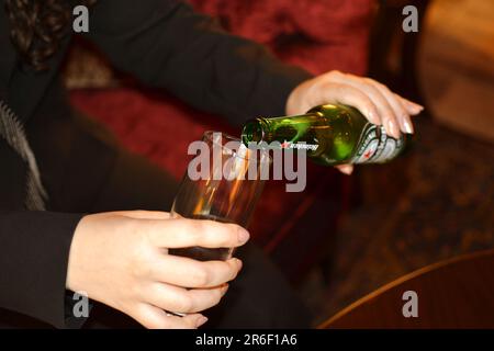 Una signora che versa la birra Heineken in un bicchiere mentre si siede in un bar Foto Stock