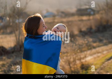 La donna abbraccia il suo piccolo figlio avvolto in giallo e bandiera blu dell'Ucraina all'aperto. Foto Stock