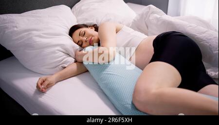 Donna incinta che dorme sul letto con il cuscino speciale Foto Stock
