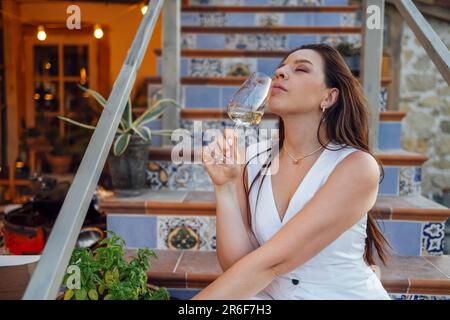 Attraente giovane donna è seduta sulla terrazza gradini di casa e bere champagne. La bella ragazza che scama tiene il bicchiere e gode di vino frizzante a ho Foto Stock