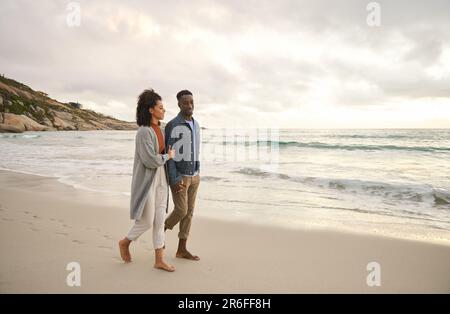 Giovane coppia multietnica che tiene le mani e cammina lungo una spiaggia Foto Stock