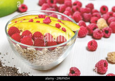 Una ciotola piena di cereali per la colazione, lamponi freschi e altri ingredienti assortiti Foto Stock