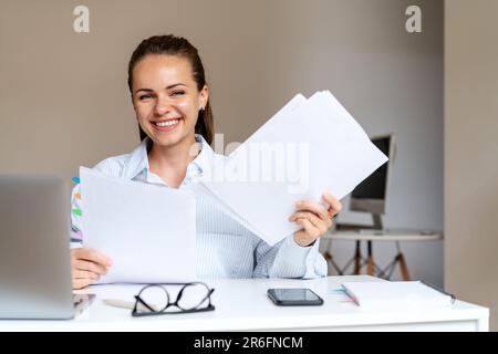 Felice giovane contabile donna sorridente mentre lavora con documenti finanziari in ufficio. Foto Stock