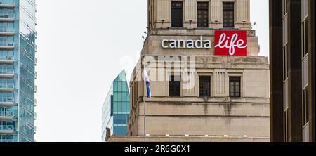 Toronto, Canada - 4 giugno 2023: Il Canada Life Building con una bandiera su un paletto. Edifici alti sono visibili sullo sfondo. Foto Stock