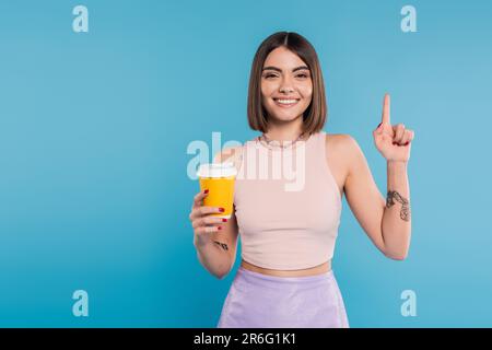 per andare a caffè, felice giovane donna con capelli corti, tatuaggi e naso piercing tenendo la tazza di carta su sfondo blu, generazione z, tendenze estive, attratti Foto Stock
