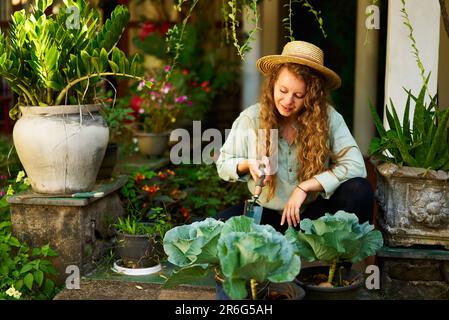 Giovane donna caucasica giardiniere piantando verdure sorridendo felicemente. Giovane donna allegra con cazzuola seduta nel suo giardino che si prende cura di vaso Foto Stock