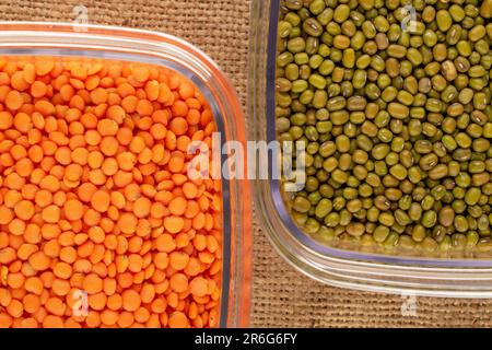 Lenticchie rosse e fagiolini in contenitori di plastica su tela di iuta, macro, vista dall'alto. Foto Stock