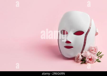 Salute e bellezza del viso. Maschera cosmetica a LED trattamento rigenerativo su sfondo rosa con delicati fiori di rosa e un posto per te Foto Stock