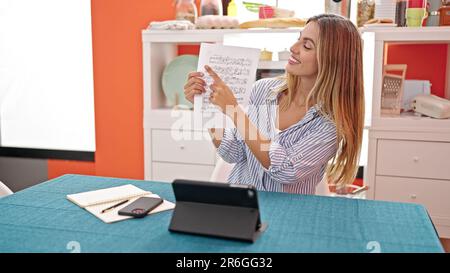 Giovane donna bionda che ha lezioni di musica online in sala da pranzo Foto Stock