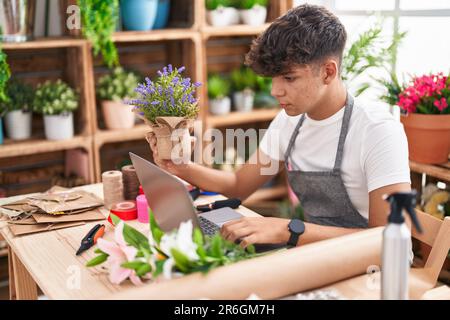 Giovane fiorista ispanico adolescente che utilizza un computer portatile che tiene la pianta di lavanda al negozio di fiori Foto Stock