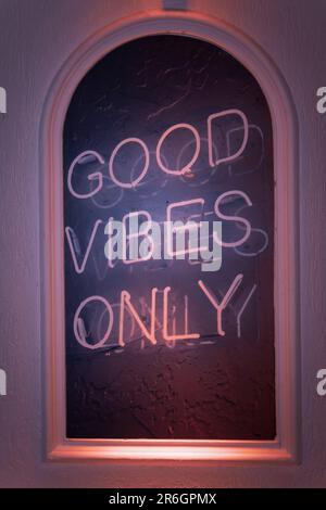 Un vivace cartello al neon con "Good Vibes Only" illuminato in una finestra Foto Stock