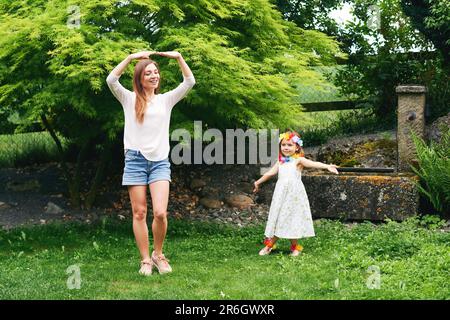 Giovane madre che balla con la figlia piccola carina in giardino, famiglia che passa il tempo insieme Foto Stock