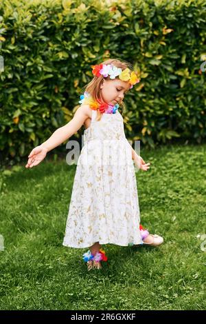 Ritratto all'aperto di adorabile bambina che gioca nel parco, indossando abiti bianchi e fiori colorati Foto Stock