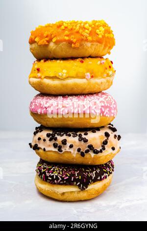 Una varietà di ciambelle colorate disposte su un tavolo su uno sfondo bianco Foto Stock