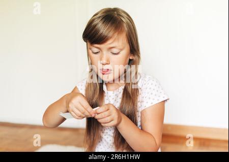 Piccola ragazza concentrata che gioca con carta nella sua stanza Foto Stock