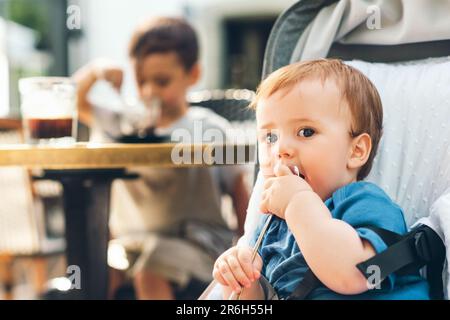 Ritratto all'aperto di un bambino felice che gioca con un cucchiaio, seduto in un buggy Foto Stock