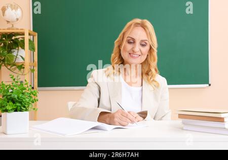 Professore che tiene una lezione vicino al green board alla scrivania in aula Foto Stock