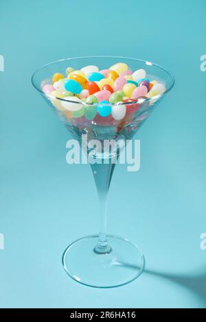 Bellissimo bicchiere martini con caramelle colorate su sfondo azzurro Foto Stock