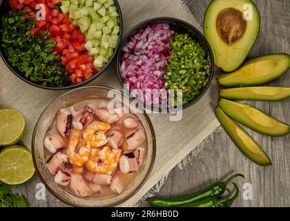 Una gamma di prelibatezze di pesce preparate al momento e ciotole di verdure a fette su un tavolo da cucina Foto Stock