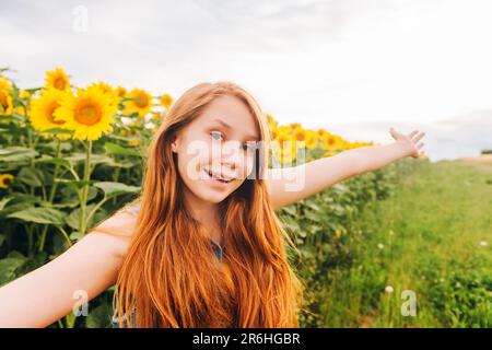 Ritratto all'aperto di ragazza carina giovane con capelli rossi in posa in campo di girasole Foto Stock