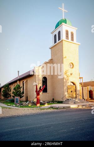 Chiesa di San Giuseppe a Cerrillos, New Mexico, con cielo azzurro, strada di fronte, e piccola luna nella luce della prima sera. Foto Stock