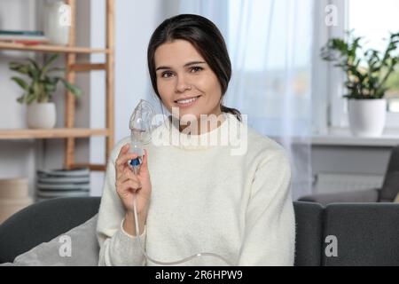 Giovane donna felice con nebulizzatore a casa Foto Stock