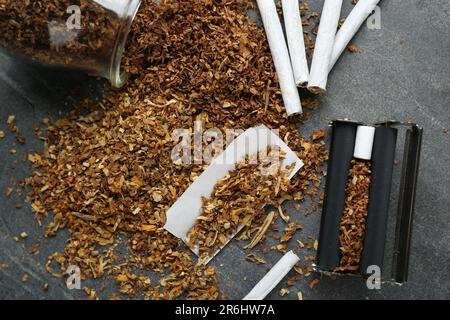 Composizione a giacitura piatta con rullo e tabacco su tavolo grigio scuro. Fare le sigarette arrotolate a mano Foto Stock