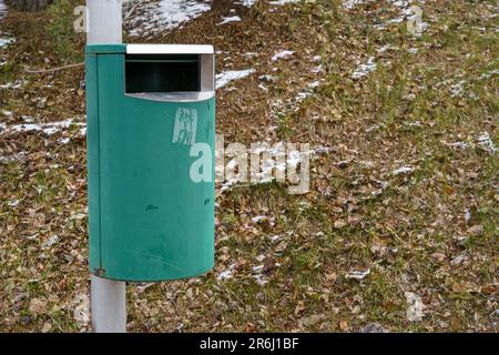 Cestino verde può su palo metallico con erba e neve sullo sfondo Foto Stock