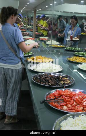 Una giovane donna sceglie il suo pasto da una selezione di cibi freschi esposti a un buffet in un ristorante israeliano. Foto Stock