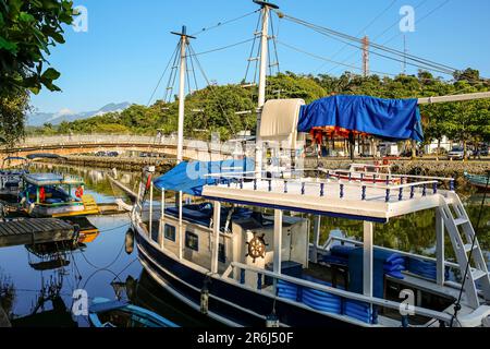 Barca turistica sul fiume Pereqe-ACU con grande sullo sfondo in una giornata di sole nella città patrimonio dell'umanità dell'UNESCO Paraty, Brasile Foto Stock