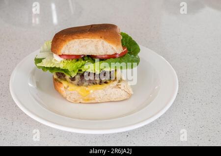 Hamburger di manzo grattugiato biologico fatto in casa con formaggio, pomodoro e lattuga su un piatto sulla panca della cucina. Foto Stock