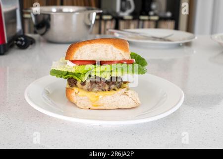 Hamburger di manzo grattugiato biologico fatto in casa con formaggio, pomodoro e lattuga su un piatto sulla panca della cucina. Foto Stock