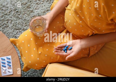 Giovane donna incinta con un bicchiere d'acqua e pillole di acido folico a casa, primo piano Foto Stock