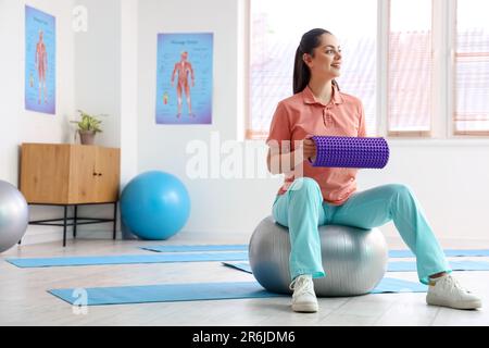 Fisioterapista femminile con rullo in gommapiuma nel centro di riabilitazione Foto Stock