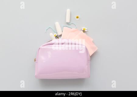 Borsa cosmetica da donna con tamponi e tamponi mestruali su sfondo grigio Foto Stock