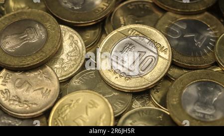 primo piano di una vecchia moneta indiana d'oro e d'argento 10 rupie in una collezione di autentiche monete da dieci e cinque rupie in pile sparse Foto Stock