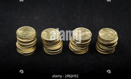 pile di oro indiano d'annata 5 o cinque rupie monete divise equamente e isolate su sfondo nero Foto Stock