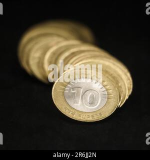 primo piano di rare monete in rupia indiana da dieci (10) d'oro e d'argento, disposte in una fila curva isolata su sfondo nero Foto Stock