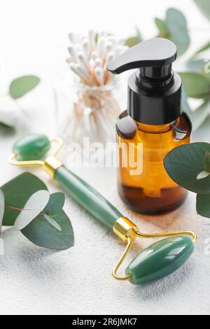 Cura naturale della pelle e aromaterapia con bottiglia di olio essenziale di eucalipto, rullo di giada di bellezza, gua sha su fondo di cemento. Spa, benessere, massaggi e Foto Stock