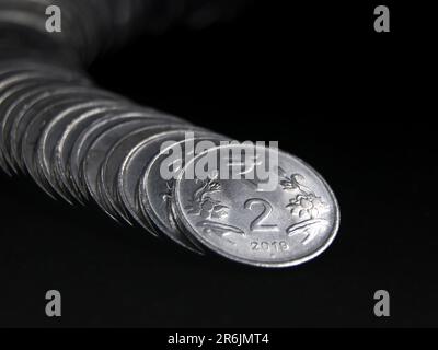 primo piano di 2 rupie d'argento monete indiane disposte e impilate in un serpente come una fila curva isolata su uno sfondo nero Foto Stock