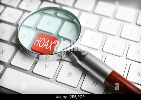 Lente d'ingrandimento su pulsante rosso con parola Hoax sulla tastiera del computer, primo piano Foto Stock