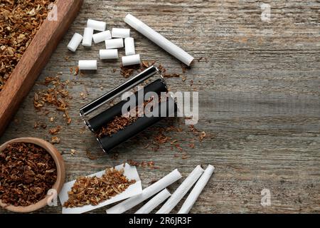 Composizione piatta con rullo e tabacco su vecchio tavolo di legno, spazio per il testo. Fare le sigarette arrotolate a mano Foto Stock